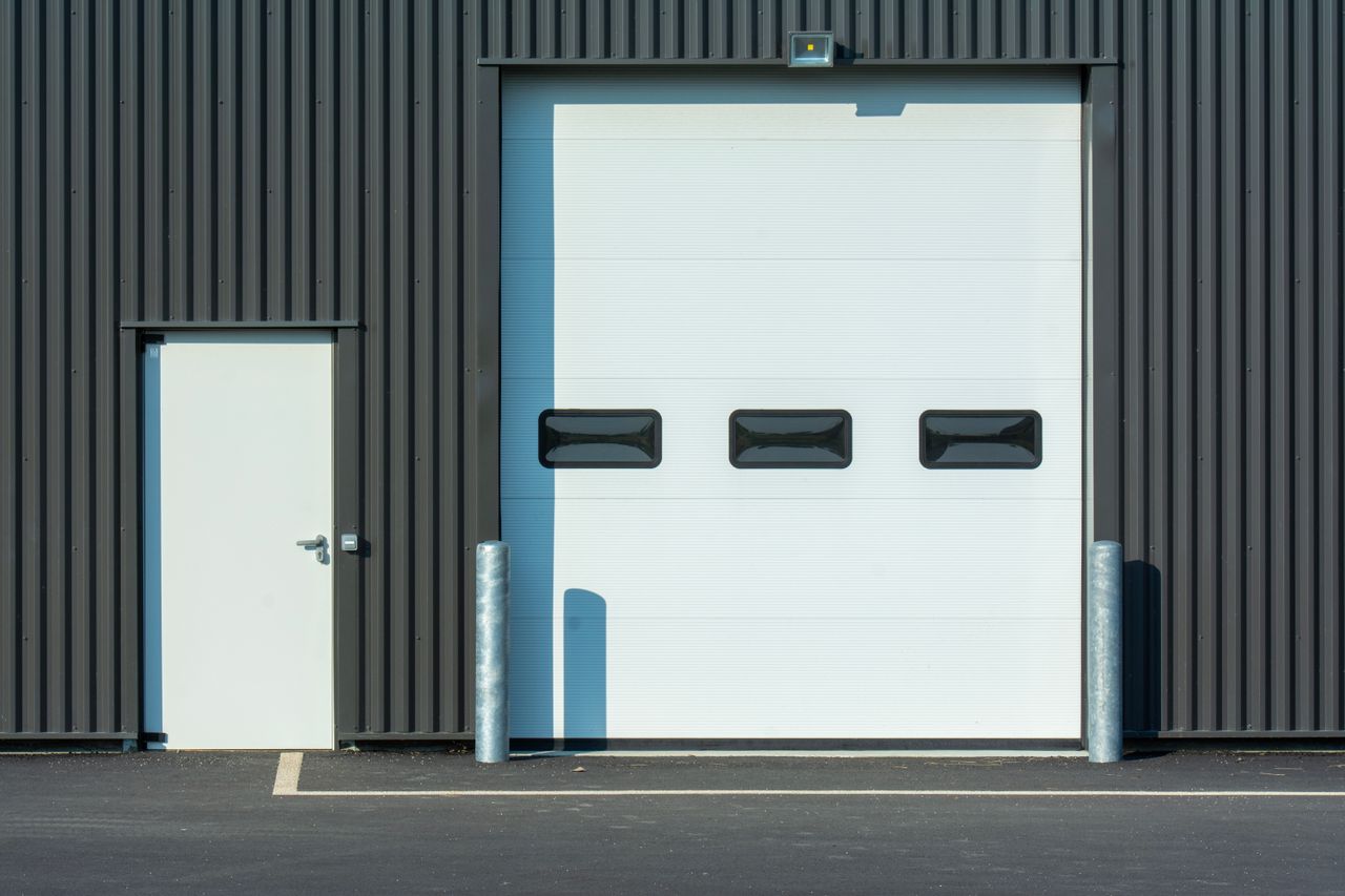 A modern industrial warehouse facade with a large white garage door and side entrance.