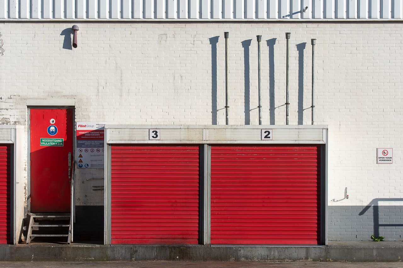 Red shutters and emergency exit on a white brick industrial building wall.