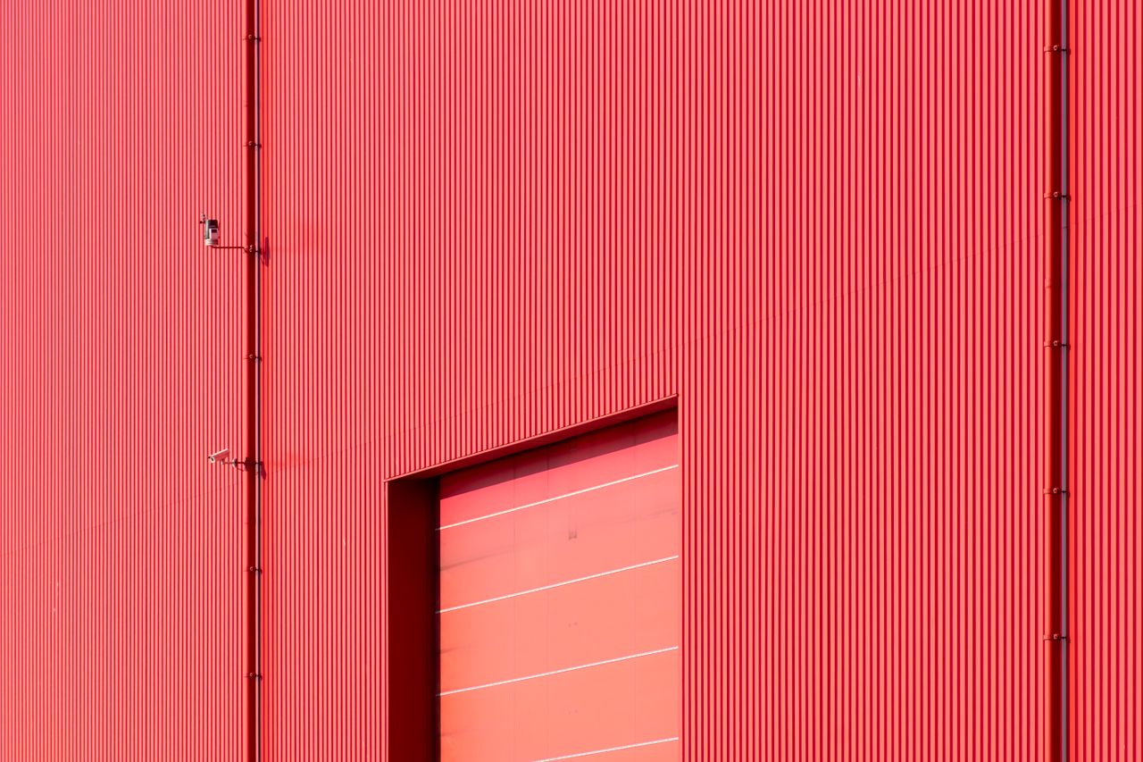 Close-up of a textured red industrial wall with a slightly open door, highlighting modern architectural design.