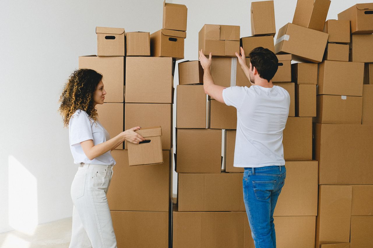 Young man and woman in casual clothes carrying and arranging cardboard boxes after receiving parcels during relocation into new light apartment